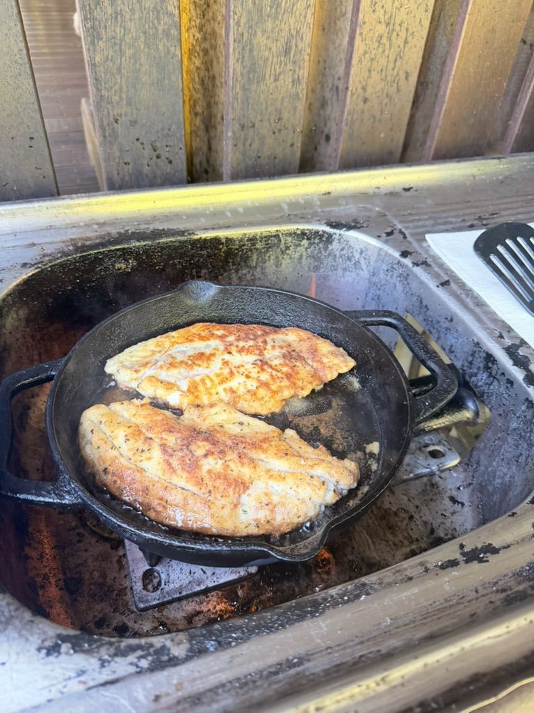 Fish fillets frying in a cast-iron pan on the camp stove